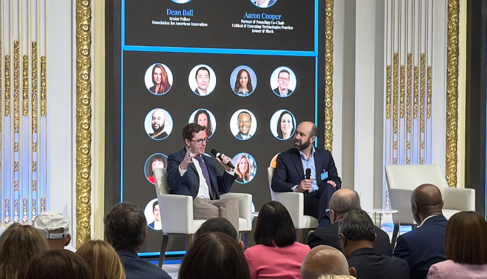 Two panelists speaking onstage before an audience at an Alpha summit.